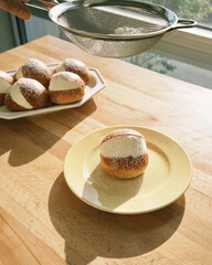 Sifting sugar over plated cream-filled bun.