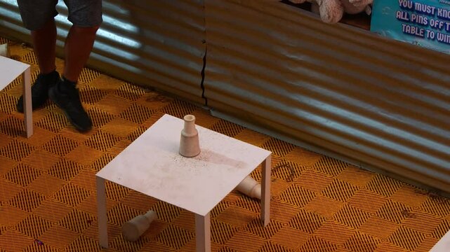 Player throwing a ball, aiming at the milk bottles stacked on the table, a classic carnival knockdown game.