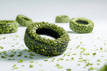 Black car tires covered in green leaves scattered on white surface symbolizing eco-friendly transportation and sustainable mobility. Copy space