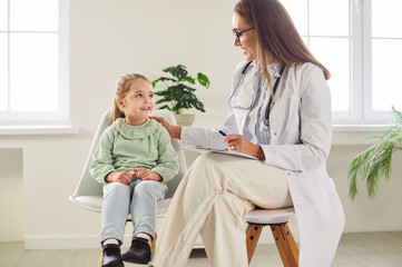 Little preschool girl sitting on chair with friendly family doctor during examination in hospital....
