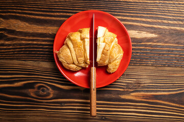 Slices of freshly baked croissants with a knife on a red plate with a wooden background. Top view