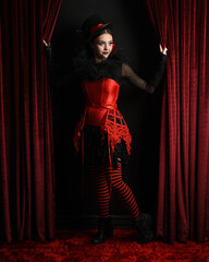 Burlesque circus performer, female model, in red corset and striped stockings in jester clown...