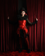 Burlesque circus performer, female model, in red corset and striped stockings in jester clown...