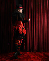 Burlesque circus performer, female model, in red corset and striped stockings in jester clown...