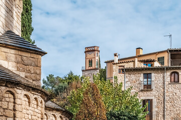 Medieval stone architecture of Girona with decorative tower, Catalan buildings, terracotta roofs, and arched details nestled in greenery under a clear blue sky, capturing the Spain historic charm