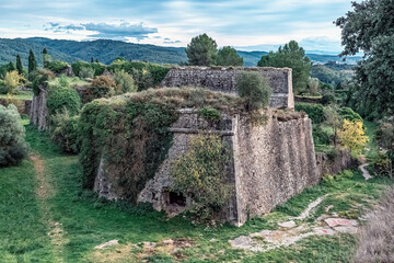 Ancient 17th-century Montjuïc Castle bastion in Girona, Spain, with angled stone walls amid greenery. Historic fortification stands against rolling mountains and blue sky, blending nature and history