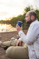 Hispanic man having breakfast, enjoying a hot drink, a freshly brewed coffee, on the bank of a...