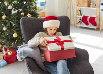 Young boy opens a gift box at home during Christmas or New Year, filled with surprise and...