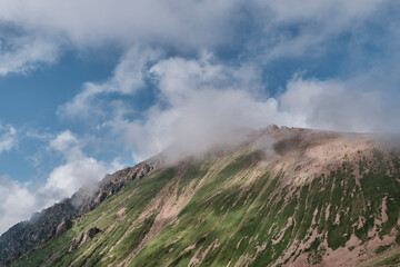 Mountain slope with green vegetation, fog and cloudy sky
