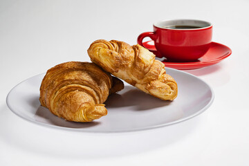 Freshly baked croissants on a plate with a cup of coffee on a white background