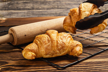 Freshly baked croissants on a cooling tray with tongs and a rolling pin on the table