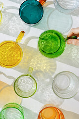 Colorful glowing glass cups on white background, casting artistic light reflections and shadows in natural sunlight. Summer drink concept, minimal trend pattern of transparent glasses, caustic
