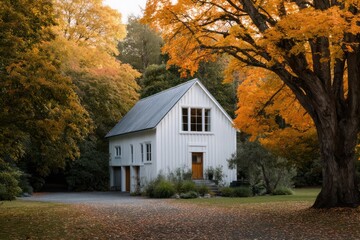 White barn-inspired house framed by autumn trees cool sidelight with soft bloom deep ambient shadows across clapboard siding
