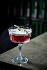A beautifully crafted cocktail sits on a marble bar, elegantly garnished with fresh rosemary
