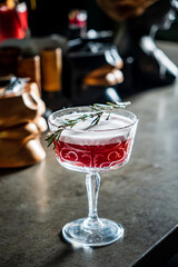 A vibrant cocktail garnished with rosemary rests on a stylish bar