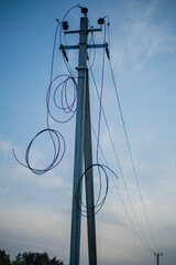 A tall power pole stands against a calm dusk sky, with tangled wires swirling and hanging