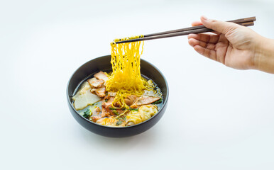 Hand picking yellow noodles from a pork noodle bowl on a white background for advertising