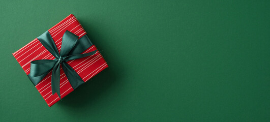 Elegant red gift box with black ribbon sits on green background evoking festivity and celebration