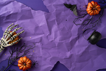 Skeleton hand, black branches, pumpkins, and a cauldron highlight this Halloween scene on purple