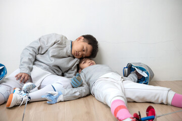 Fencer boy and girl sit on the floor with their backs against a wall, exhausted after a practice or...