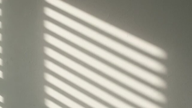 Sunlight streams through blinds casting parallel shadows on a pale wall