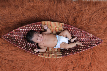 Cute Indian baby lying on a soft textured brown rug, wearing a diaper and traditional black thread...