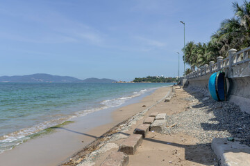 A beach with a sandy shore, calm sea, palm trees, a stone wall, and a round boat under a clear sky.