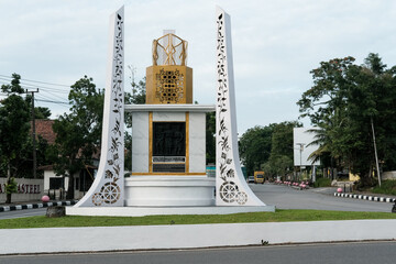 Modern white-and-gold monument standing proudly in a city roundabout, honoring local hero Depati...