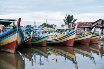 Traditional Indonesian wooden fishing boats rest quietly on calm river waters, their vivid colors reflecting a rich maritime heritage.