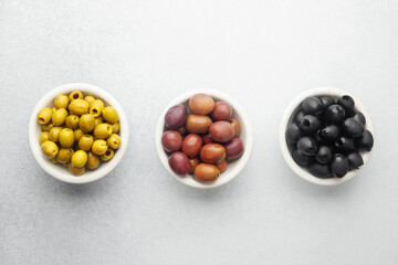 Variety of olives in bowls with wooden spoons on gray background, green olives, black and kalamata olives.