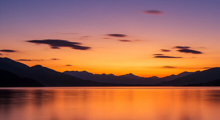 Fototapeta premium Golden Reflections: Sunset Sky Over a Mountain-Lined Lake