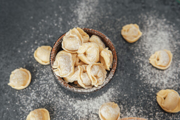 Homemade cappelletti pasta in wooden bowl with scattered pieces on table