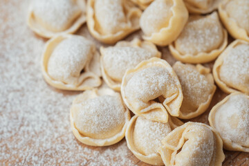 Closeup view of raw flour-dusted cappelletti pasta on wooden surface