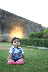 Charming baby boy dressed in a stylish blue and white outfit with a bow tie, sitting inside a decorative woven basket on green grass