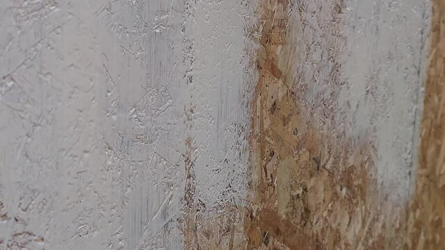 Close-up of a wooden wall being painted. The surface shows a mix of white and natural wood textures. Paint is applied unevenly, revealing the wood grain beneath.
