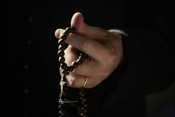 Man holding wooden rosary beads with cross in hand, wearing gold ring, standing inside church,...