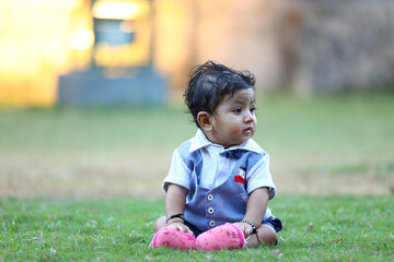 Charming baby boy dressed in a stylish blue and white outfit with a bow tie, sitting inside a decorative woven basket on green grass