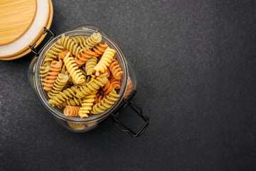 Colorful pasta in a glass jar on a dark countertop