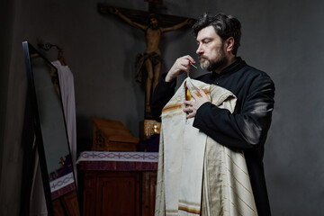 Middle aged Caucasian man with beard wearing priest robe standing in church holding liturgical...