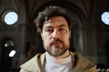 Portrait of middle aged Caucasian man wearing clerical robe standing in church looking directly at...
