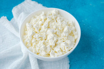 bowl of fresh cottage cheese on blue background with white napkin
