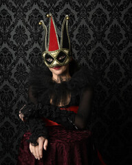 Close-up glamour portrait of masked circus burlesque model wearing jester mask, top hat, gothic...