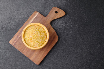 Cracked wheat groats in wooden bowl on black background. Healthy raw cereal grains.