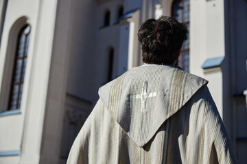 Man standing with back to camera wearing religious vestment with cross symbol, positioned outside...