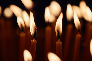 Closeup of multiple burning candles arranged together in church setting, flames flickering in...