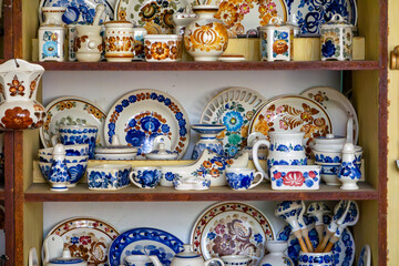 Shelf with traditional folk pottery – plates, mugs, jugs, and cups decorated with colorful floral patterns. Rustic style, element of a countryside kitchen.