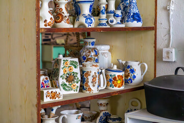 Shelf with traditional folk pottery – plates, mugs, jugs, and cups decorated with colorful floral...