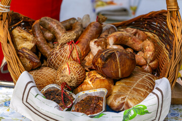 Traditional basket with regional smoked meats and cheeses – sausages, hams, smoked bundz, and lard displayed on a linen cloth, perfect for a food fair or farmers' market.