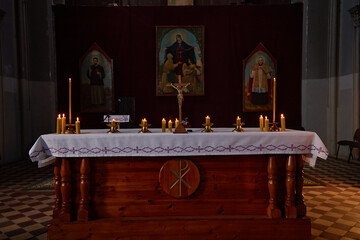 Empty church altar standing in front of religious paintings with lit candles and crucifix arranged...