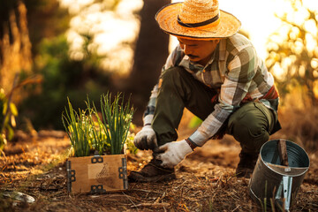 A gardener ties his shoelaces next to a potted plant.